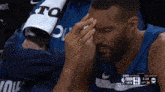 a basketball player is sitting in the stands with his hand on his forehead during a game