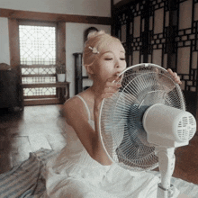 a woman in a white dress is sitting on the floor with a fan