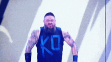 a bearded wrestler wearing a black tank top with the letter k on it
