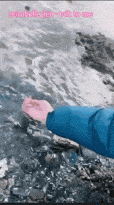 a person in a blue jacket is reaching into a body of water