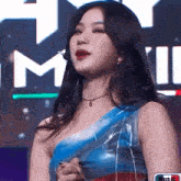 a woman wearing a blue one shoulder top is standing in front of a sign that says music .