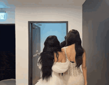 two women standing next to each other in a hallway with an exit sign on the wall