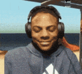 a man wearing headphones and a blue adidas sweatshirt smiles with his eyes closed