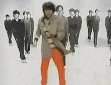 a man in a trench coat is dancing in front of a crowd of people .