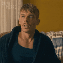 a man with a mustache is sitting on a couch with saint pierre written on the wall behind him