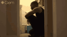 a man squatting down in a bathroom with a gem logo on the wall