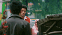 a man in a leather jacket stands next to a man in a red vest