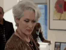 a woman with gray hair is wearing a necklace and earrings and looking down .