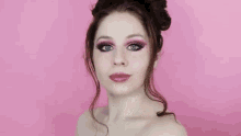 a woman with pink eye shadow is covering her mouth with her hand on a pink background .