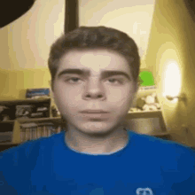 a young man wearing a blue shirt is looking at the camera in a room .