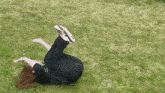 a woman is laying on her back in the grass with her feet up .