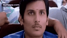 a man with a mustache is sitting in a chair and looking at the camera with a surprised look on his face .