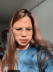 a woman wearing glasses and a blue shirt has a purse around her neck