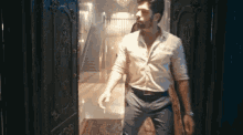 a man in a white shirt and blue pants is standing in front of a door .