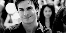 a man is smiling in a black and white photo with a crowd of people in the background .