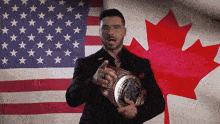 a man in front of an american flag and a canadian flag holding a trophy