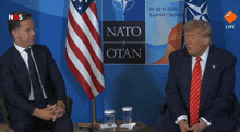 two men are sitting in front of a sign that says nato