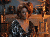 a woman in a silver sequined dress stands in front of a fireplace