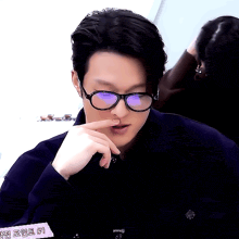 a man wearing glasses and a black jacket has a pink sign behind him that says annitj