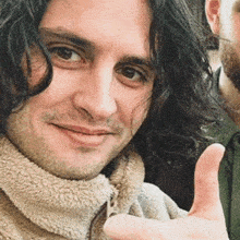 a close up of a man with long hair giving a thumbs up