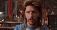 a man with long hair and a beard wears a blue shirt