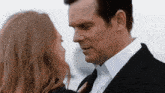 a man in a suit and a woman in a white shirt are looking into each other 's eyes