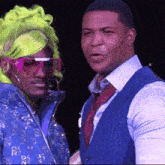 two men are standing next to each other and one is wearing a green wig and sunglasses