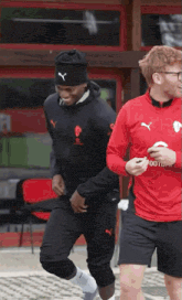 a man wearing a red shirt that says foot is walking with another man