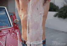 a shirtless man is being washed by a red car and the website gifrun.com is visible