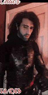 a man with long hair and a beard is standing in front of a door and holding a sword .