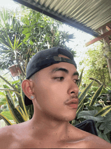 a shirtless man wearing a baseball cap and earrings looks at the camera