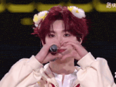 a person with red hair making a heart shape with their hands in front of a microphone