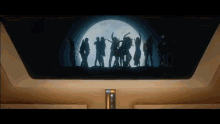a group of people are standing in front of a full moon in a dark room .