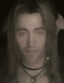 a close up of a man 's face with long hair and a necklace .
