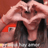 a woman is making a heart shape with her hands and the words aqui hay amor are below her