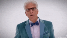 a man in a blue suit and bow tie is looking at the camera .