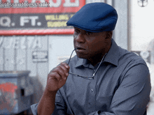a man wearing a blue hat and glasses stands in front of a sign that says q.ft.