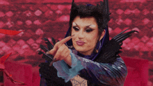 a drag queen is wearing a purple and blue costume with black feathers