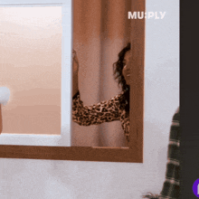 a woman in a leopard print shirt is peeking out from behind a mirror with the words murply on the bottom