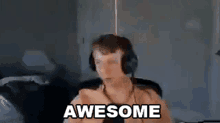 a man wearing headphones is giving a thumbs up and the words awesome are visible behind him .