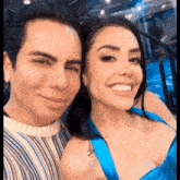 a man and a woman are posing for a picture and smiling . the woman is wearing a blue dress .
