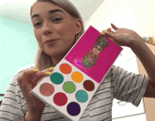 a woman in a striped shirt is holding a palette of eyeshadow