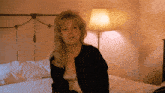 a woman sitting on a bed with a lamp in the background