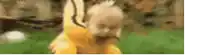 a baby in a yellow costume is walking on a green field .