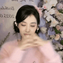 a woman in a pink sweater stands in front of flowers and a sign that says ' birthday '