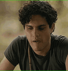 a young man with curly hair is wearing a black t-shirt and looking down .