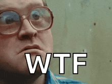 a man wearing glasses is making a funny face and the word wtf is on the screen .
