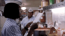 a woman in a blue and white striped shirt is looking at a menu in a restaurant kitchen