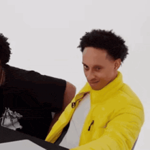 a man in a yellow jacket is sitting at a table with another man