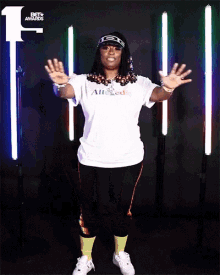 a woman wearing a white alleged t-shirt stands in front of a row of lights